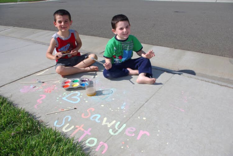 kids sitting on pavement with sidewalk chalk paintings