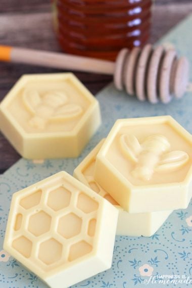 Yellow honeycomb shaped milk and honey soaps on a blue background with wooden honey dipper in background