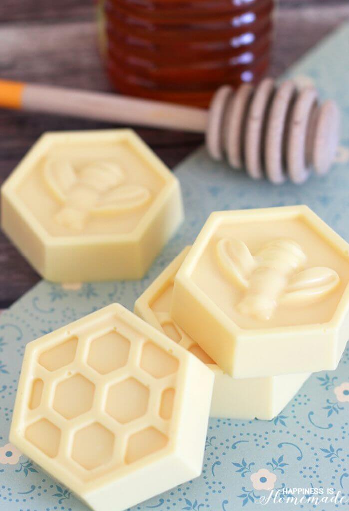 Yellow honeycomb shaped milk and honey soaps on a blue background with wooden honey dipper in background