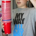 a young boy holding a stack of red cups for 'Movin On Up' Minute-to-Win-It party games