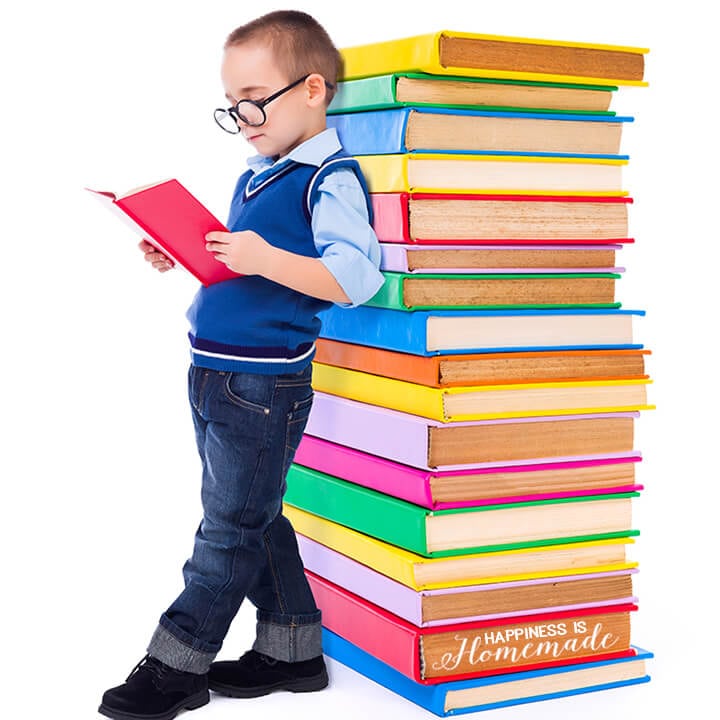 boy leaning on tower of books while reading a book