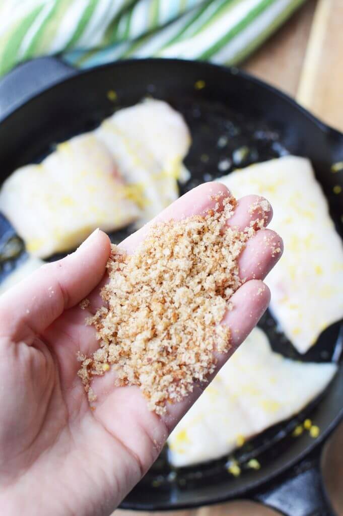 bread crumbs in hand over skillet of haddock