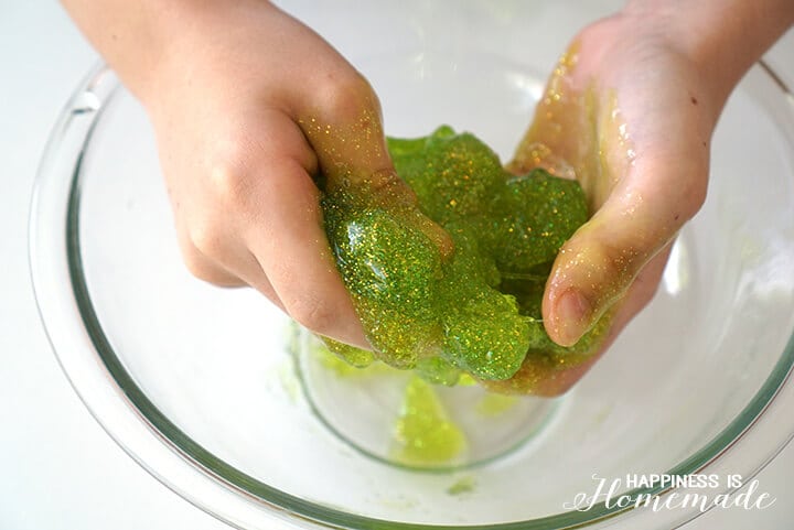 hands molding green slime in bowl