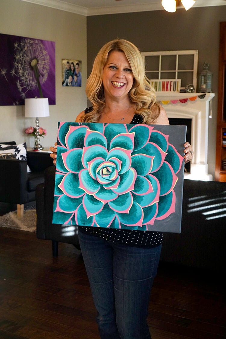 girl smiling holding up her beautiful succulent painting done at wine and paint party