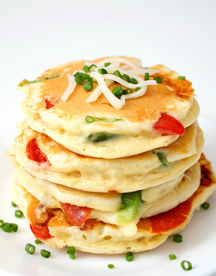 stack of pizza pancakes on a white background with pepperoni, bell peppers, cheese, and green onions
