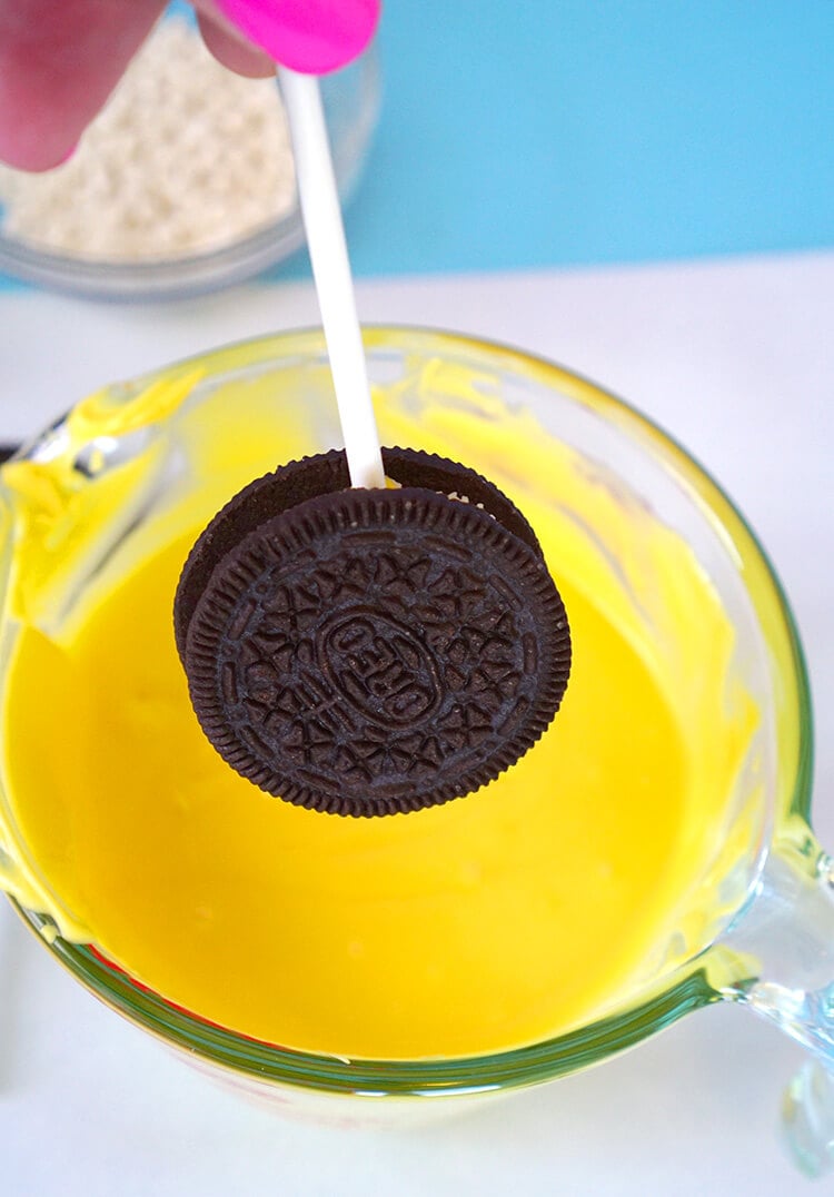 oreo on a stick being dipped into melted yellow candy melt