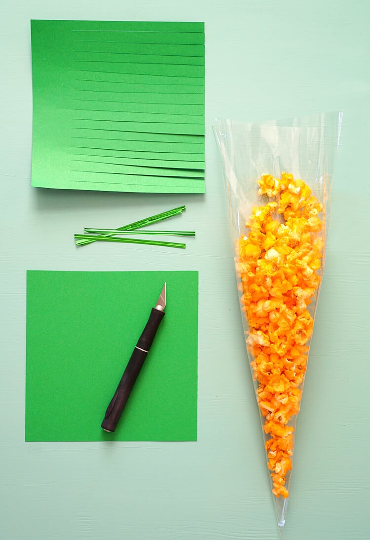 popcorn filled inside of treat bag next to sheets of green paper