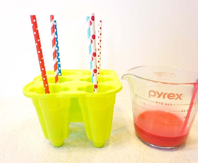 sticks inserted into rocket pop molds with measuring cup next to it