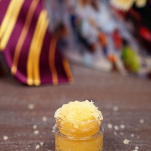 Small jar of Butterbeer sugar scrub on wood background with Harry Potter book and Gryffindor tie in background