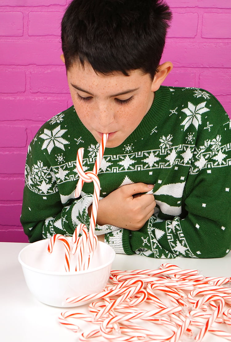 young boy using candy cane in mouth to pick up more candy canes 