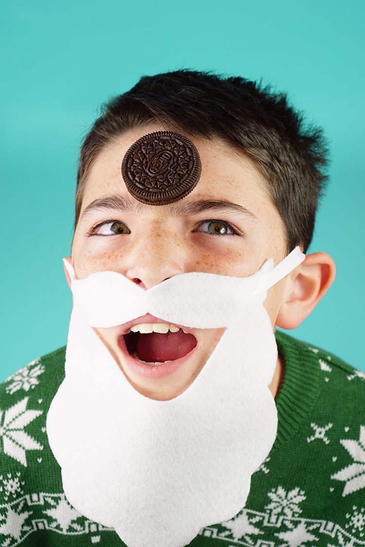 kid balancing oreo on his forehead wearing paper santa beard
