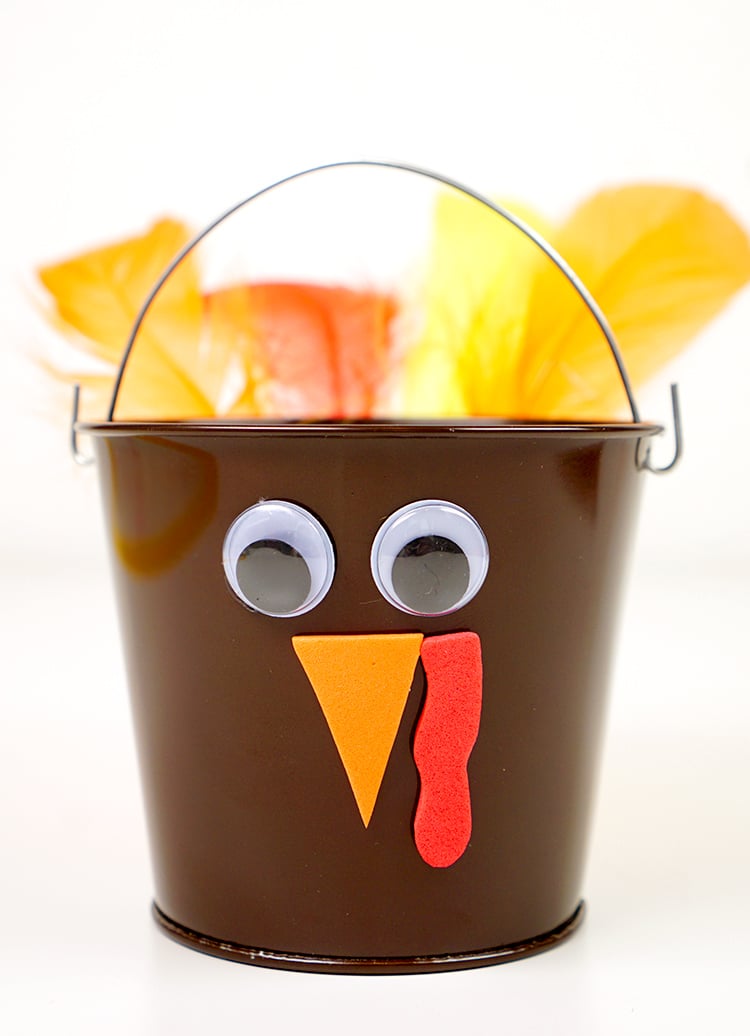 feathers glued to back of bucket and googly eyes and face added to front of turkey treat bucket