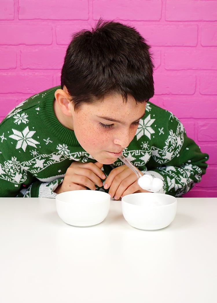 kid balancing marshmallows on spoon hanging out of his mouth trying to get them into a bowl