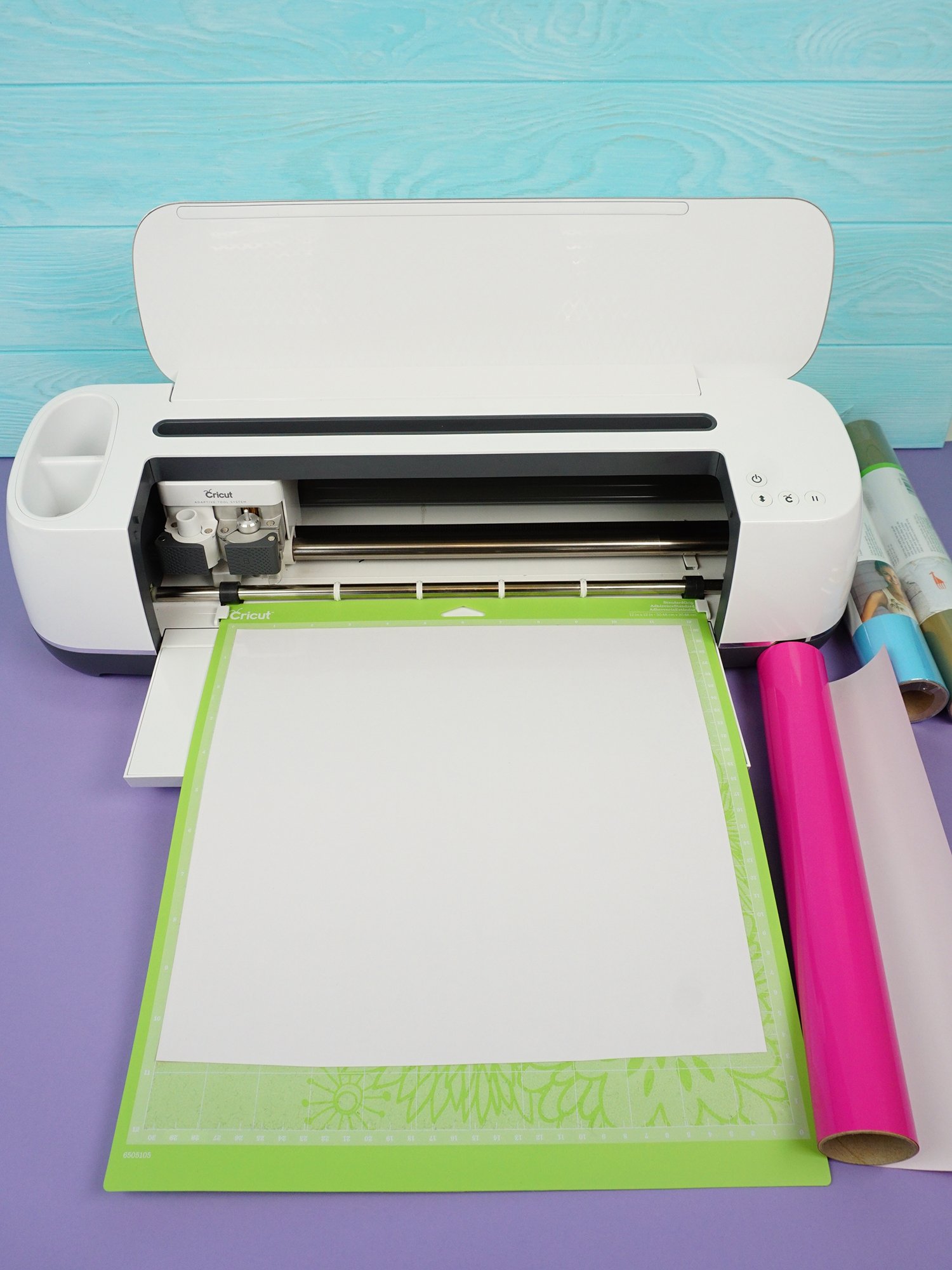 Cricut Maker machine cutting white iron-on vinyl on green mat on purple background