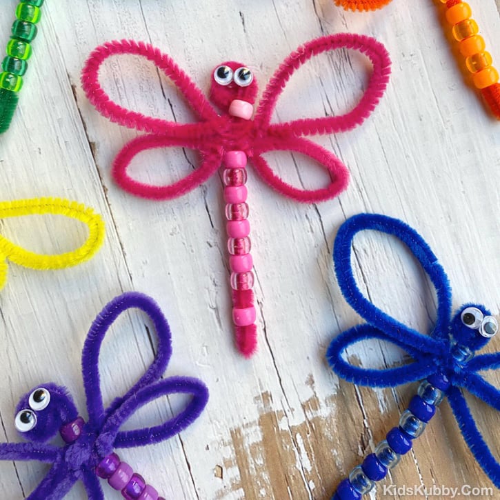Colorful dragonflies made from pipe cleaners and beads on white wood background