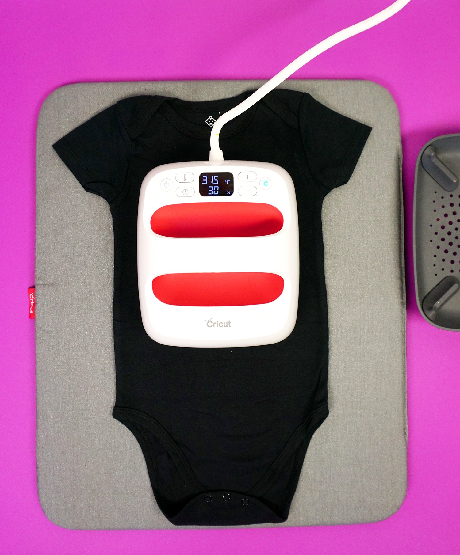 Cricut 6x7 EasyPress 2 on a black baby bodysuit on EasyPress mat and purple background