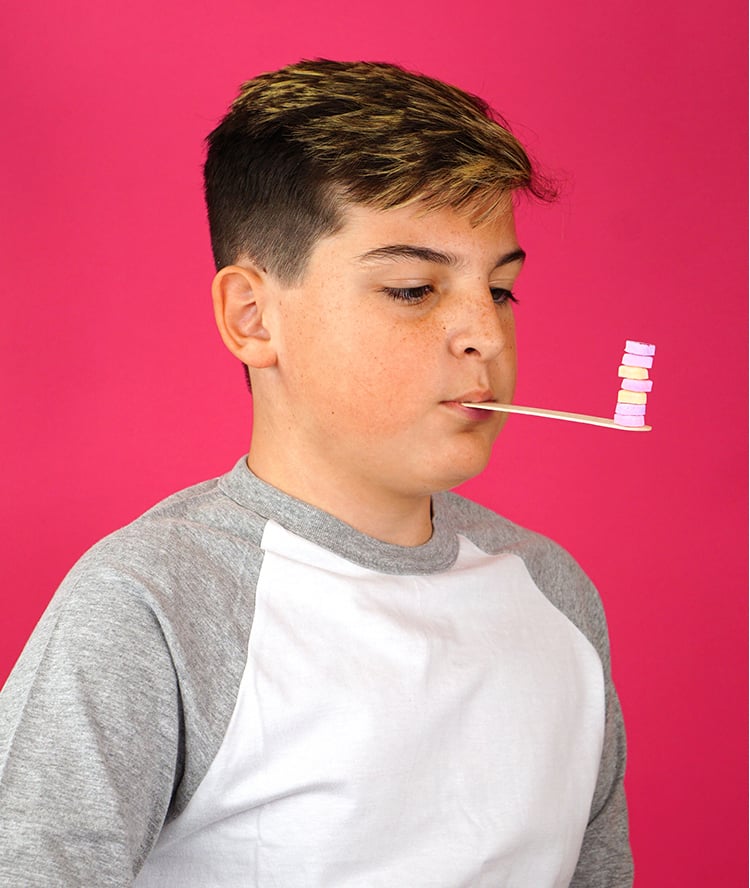 boy balancing conversation hearts on craft stick being held in mouth