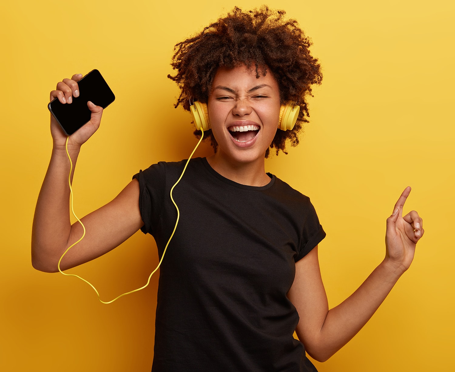 Girl listening to music with headphones on yellow background