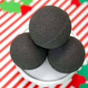 A Close Up of 4 Stacked "Lump of Coal" Bath Bombs on a Red and White Striped Background