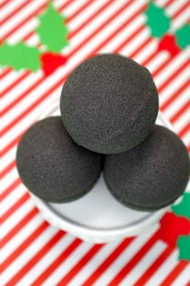 A Close Up of 4 Stacked "Lump of Coal" Bath Bombs on a Red and White Striped Background