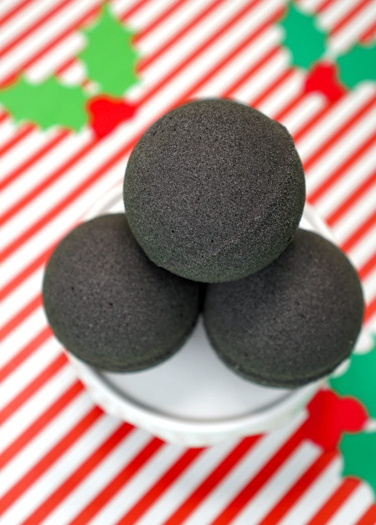 A Close Up of 4 Stacked "Lump of Coal" Bath Bombs on a Red and White Striped Background