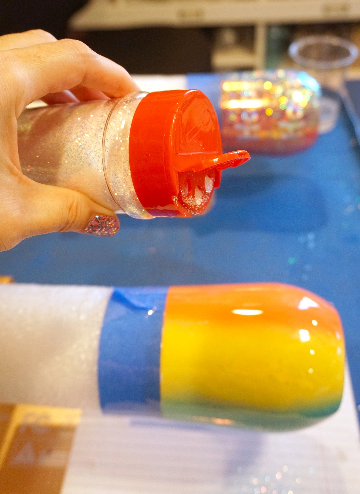 pouring glitter onto the rainbow painted tumbler