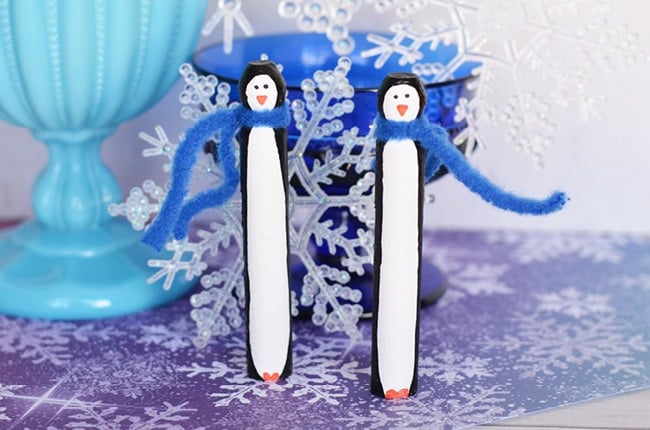 two penguins made from doll pins standing next to each other on a table