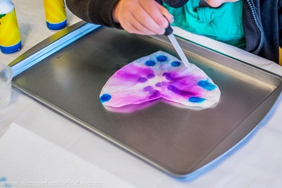 child playing with coffee filter heart craft on tray with eyedropper full of colors