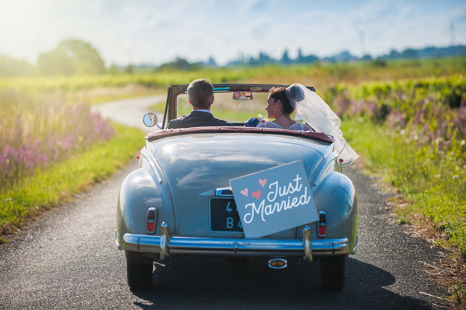 married couple driving away with just married sign on back of car