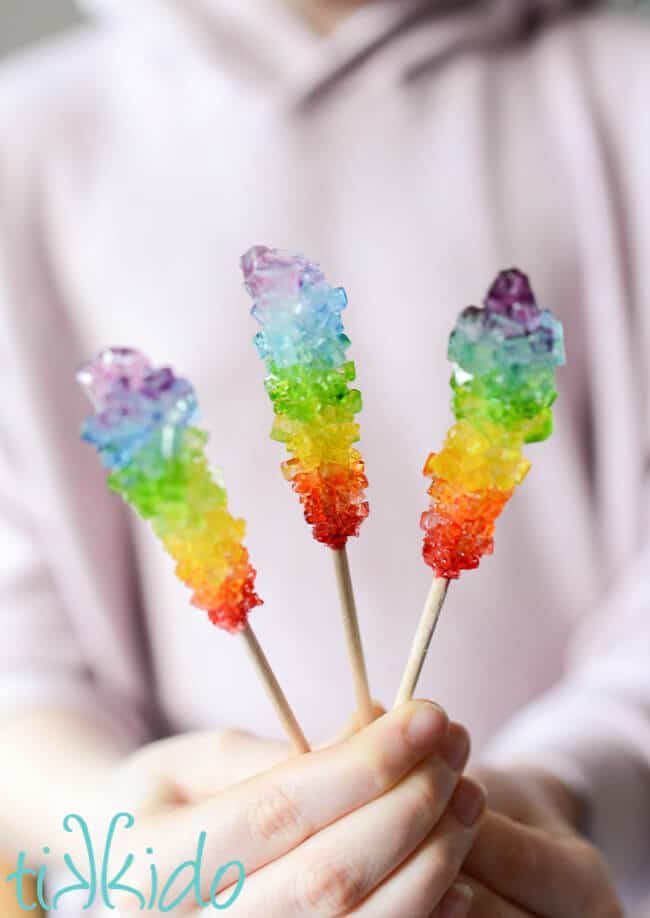 hand holding three rainbow rock candies on sticks