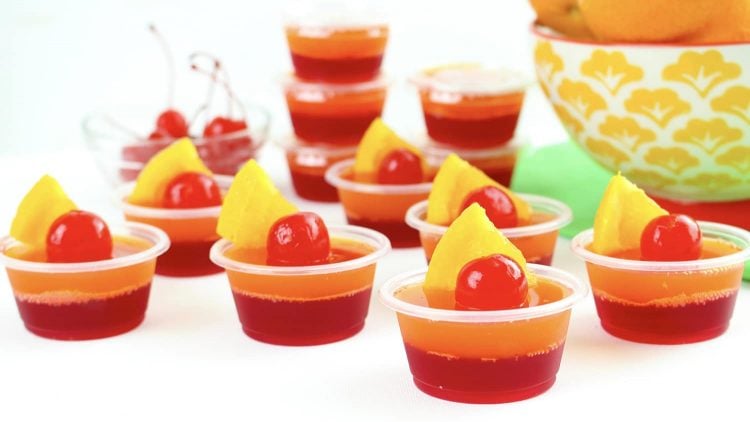 Tequila Sunrise Jello shots with cherry and pineapple garnishes on a white table