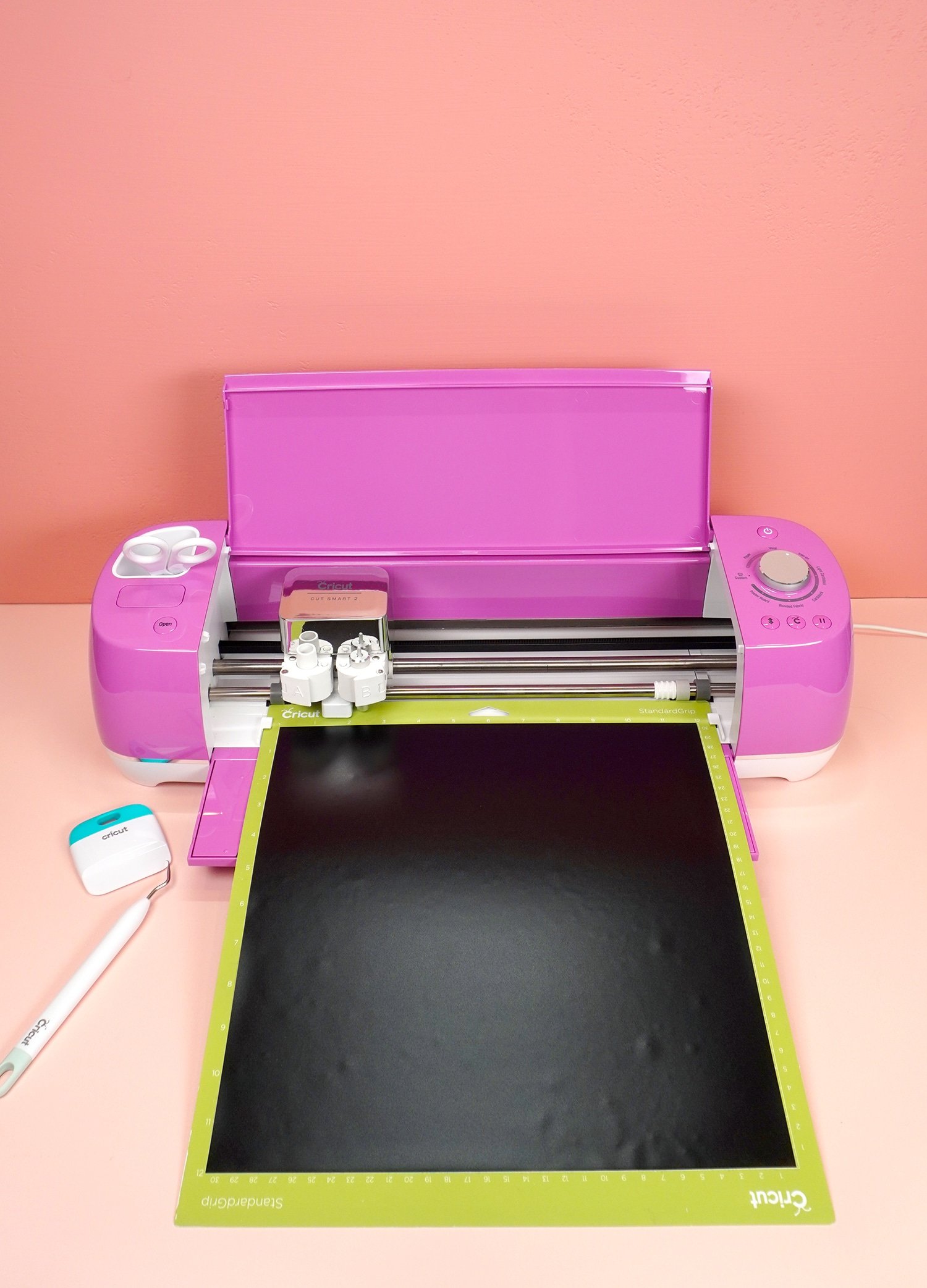 Fuchsia Cricut Explore Air 2 machine with mat and black vinyl, scraper tool, and weeding hook