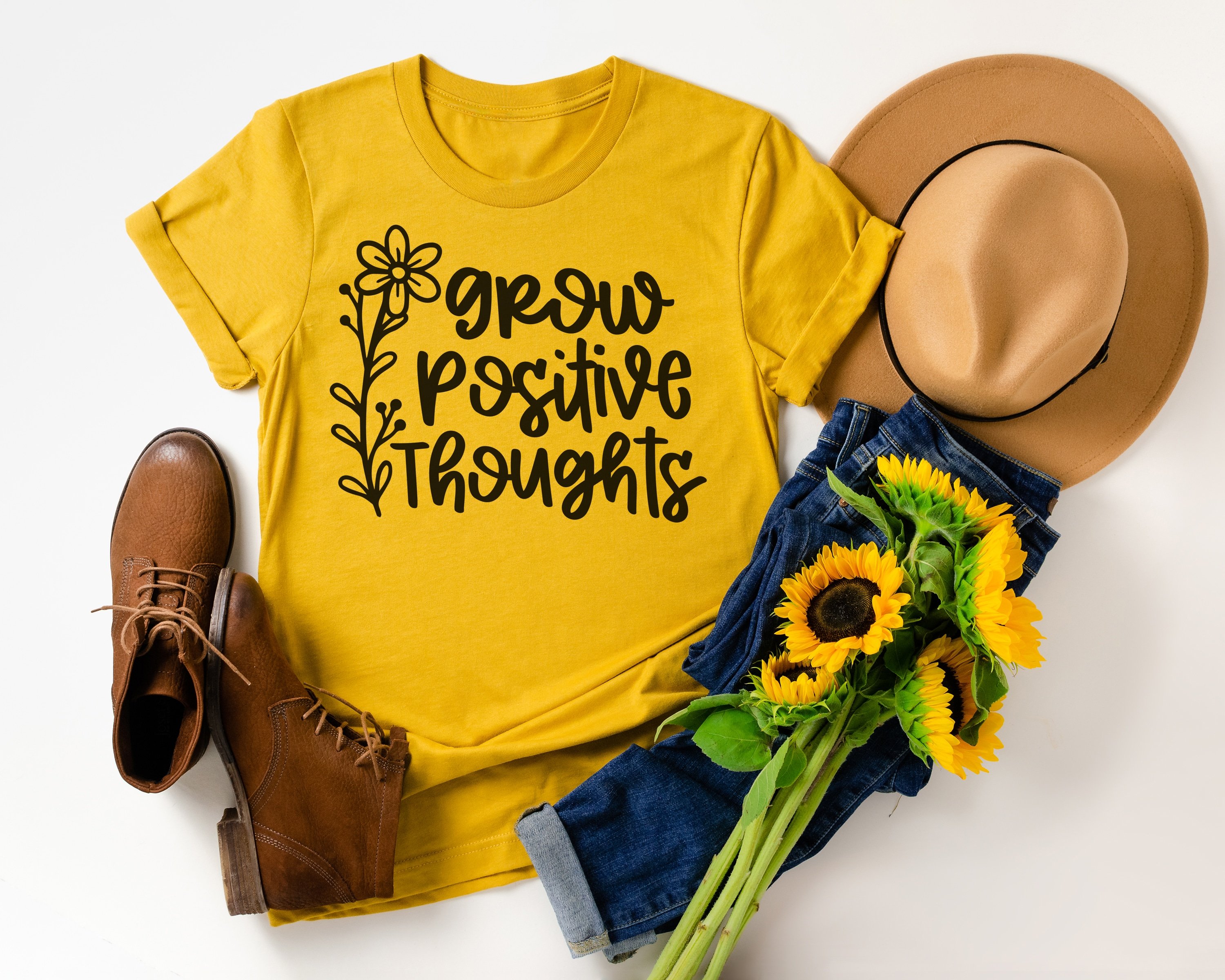 "Grow Positive Thoughts" on mustard yellow shirt with styled outfit, hat, and sunflowers