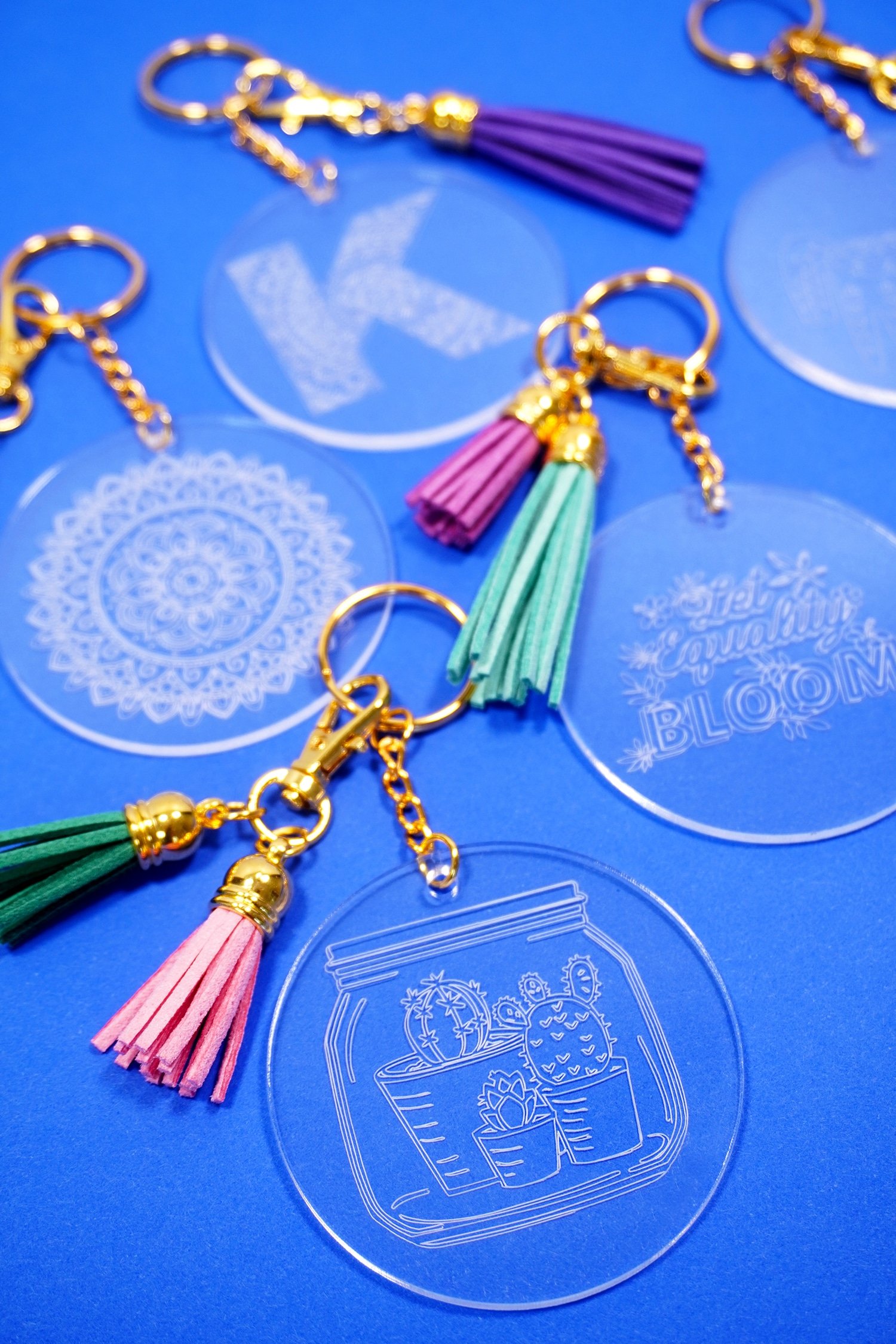 Engraved acrylic keychains with tassels on a blue background made with Cricut Maker Engraving Tool