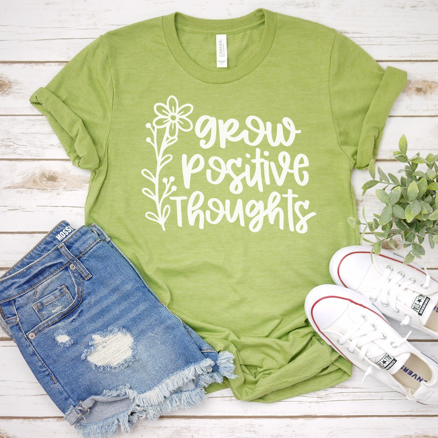 Green t-shirt featuring grow positive thoughts message across front, with white shoes and blue jean shorts 