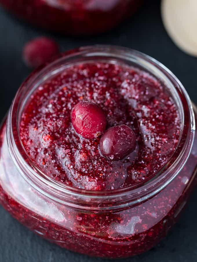 Close up of cranberry sugar scrub in jar with two whole cranberries on top