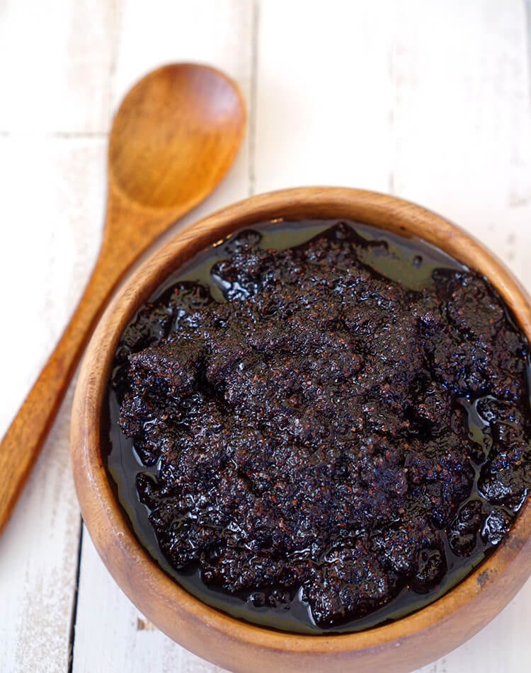 Close up of coffee sugar scrub in a wooden bowl with a wooden spoon on a white wood background