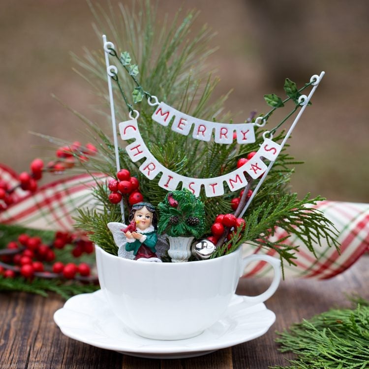 White tea cup with fairy figurine, faux cranberry decoration, and small Merry Christmas banner inside