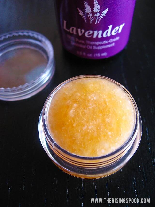 Small jar of honey lavender lip scrub with lavender essential oil bottle in background