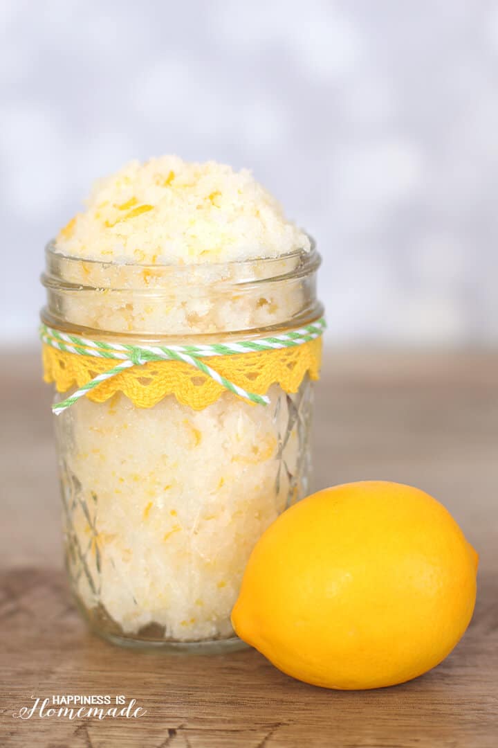 Glass jar of pale yellow lemon-lime coconut sugar scrub with a lemon in front on a wood background