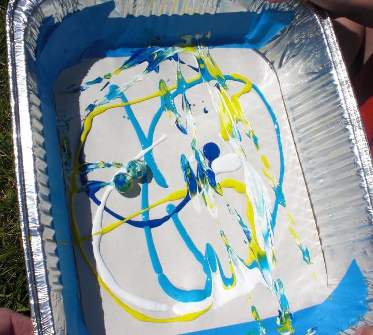 Marbles rolling around in tin tray with paint splattered in tray