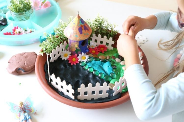 Hand painted round fairy garden house with white picket fences around it in terra cotta pot