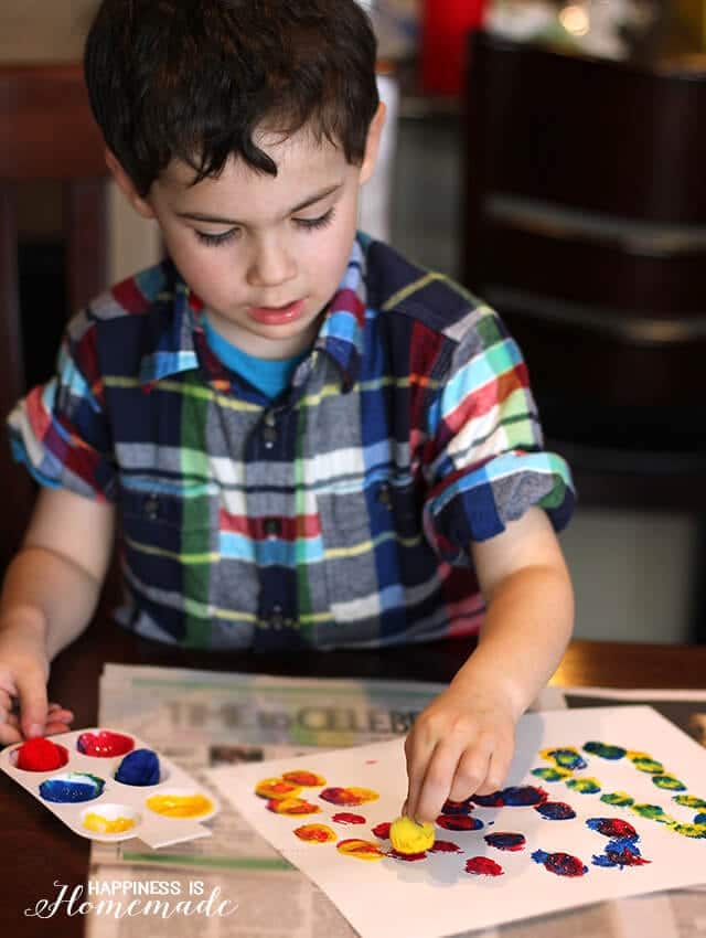 Child painting picture using pom-pom craft materials