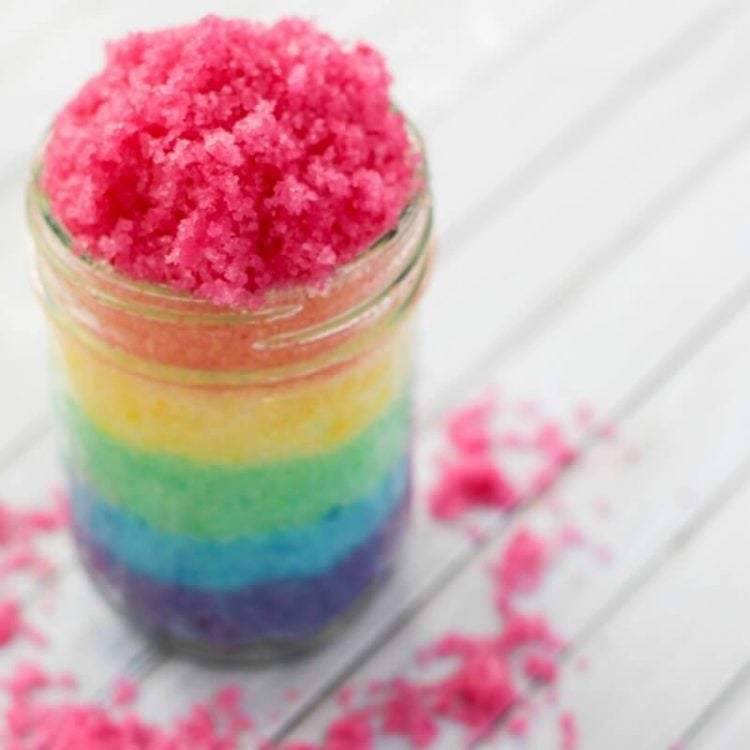 Jar of layered rainbow sugar scrub on wood background