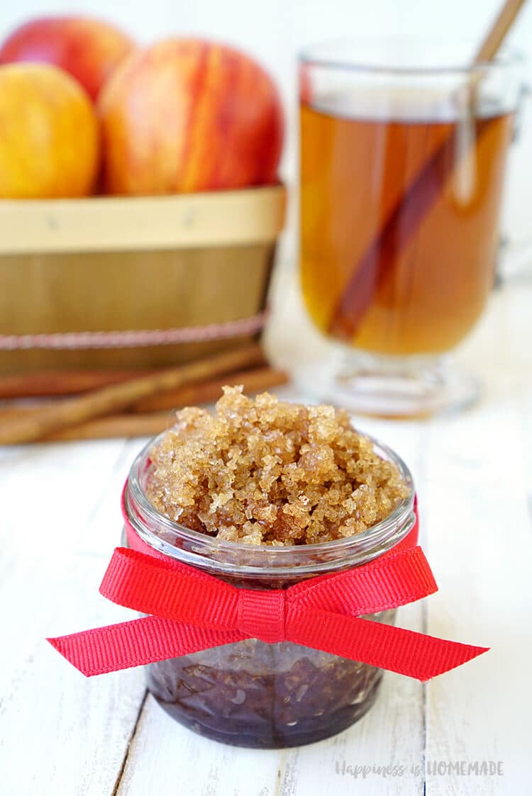 Small glass jar of spiced apple cider brown sugar scrub with a red bow and apples and cider in background