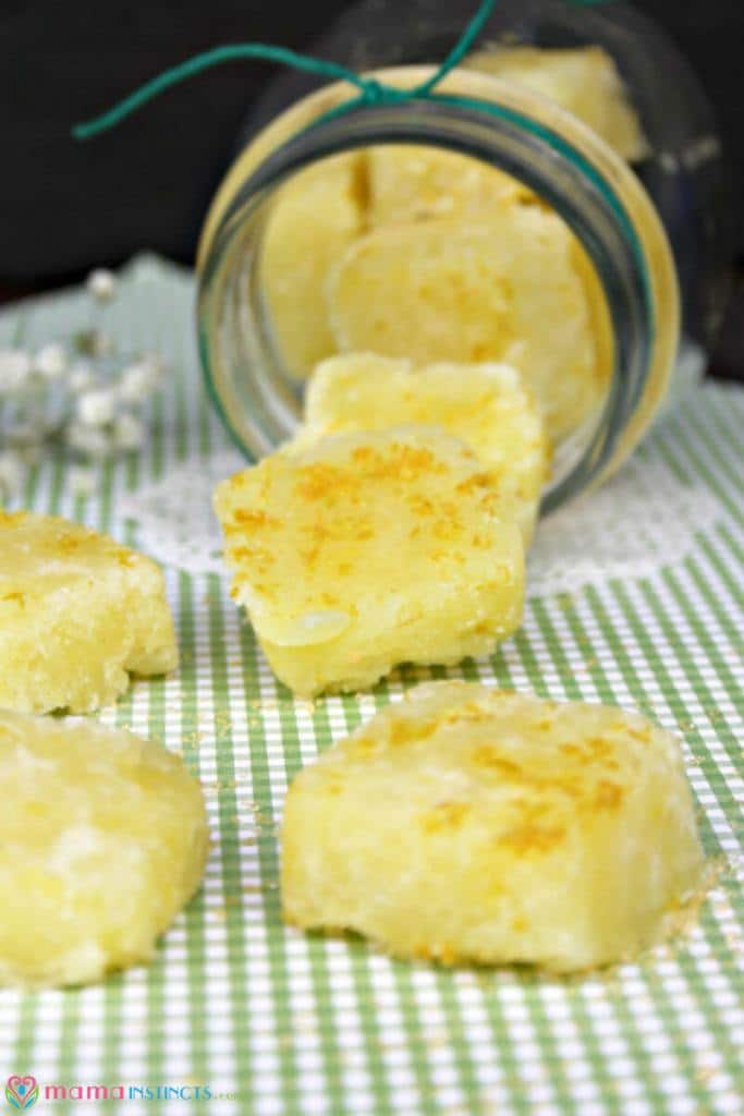 Yellow sugar scrub cubes spilling from glass jar on to green gingham checked background