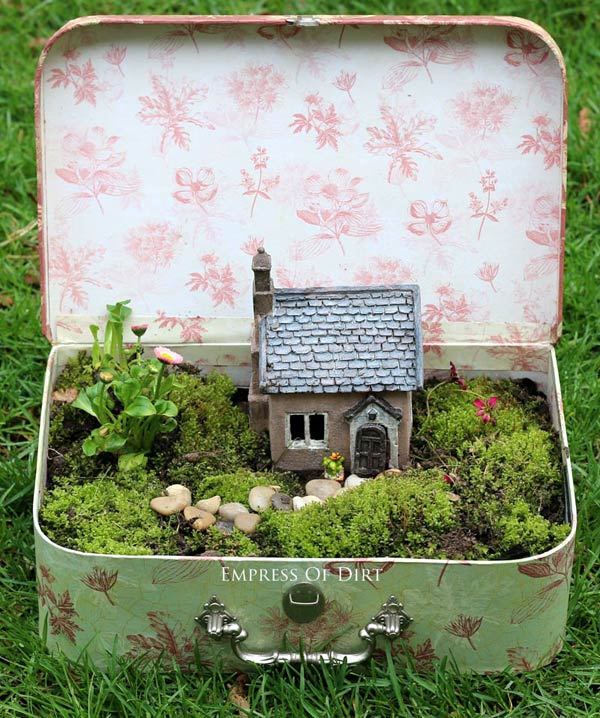 Fairy garden in a recycled suitcase filled with greenery and a small fairy house
