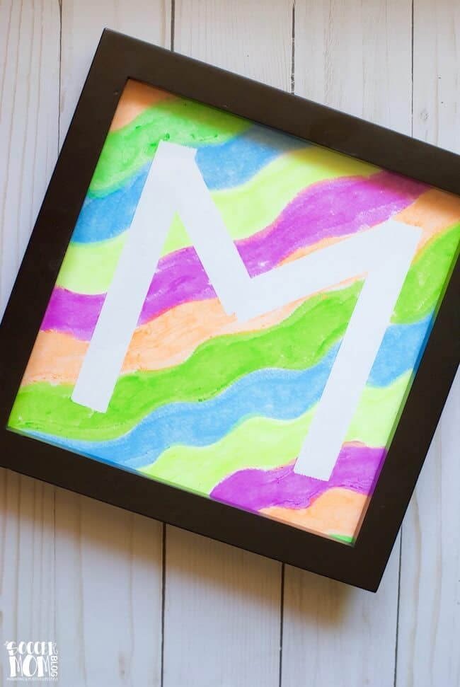 Initial 'M' in white over painted layered background in photo frame