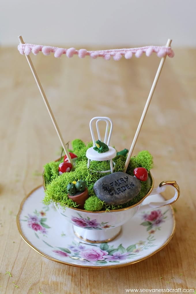 DIY fairy garden in a teacup with banner and miniature chair
