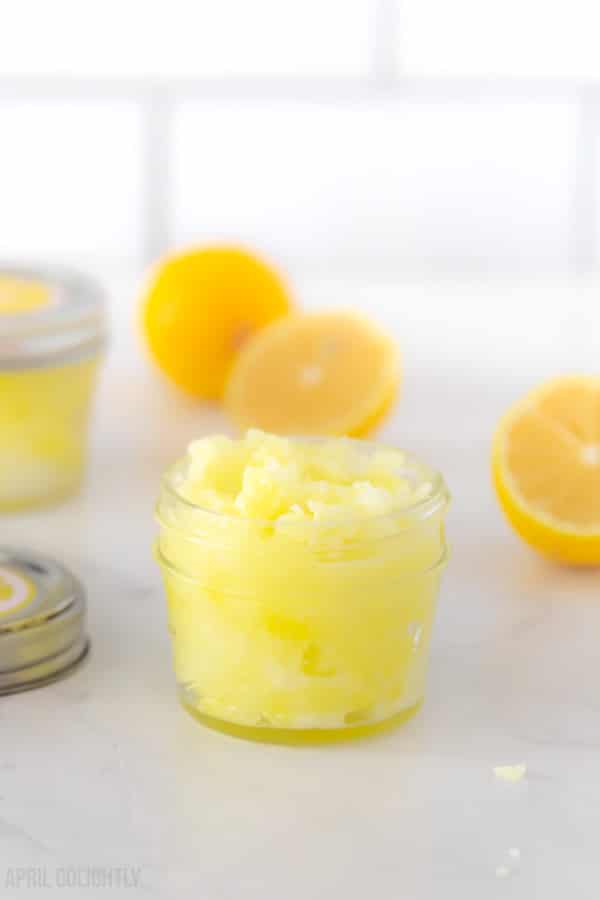 Small jar of yellow lemon sugar scrub with lemon slices in the background